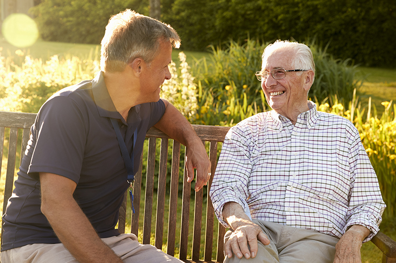 Two elderly individuals are sitting on a bench, laughing together in Denison, Texas.